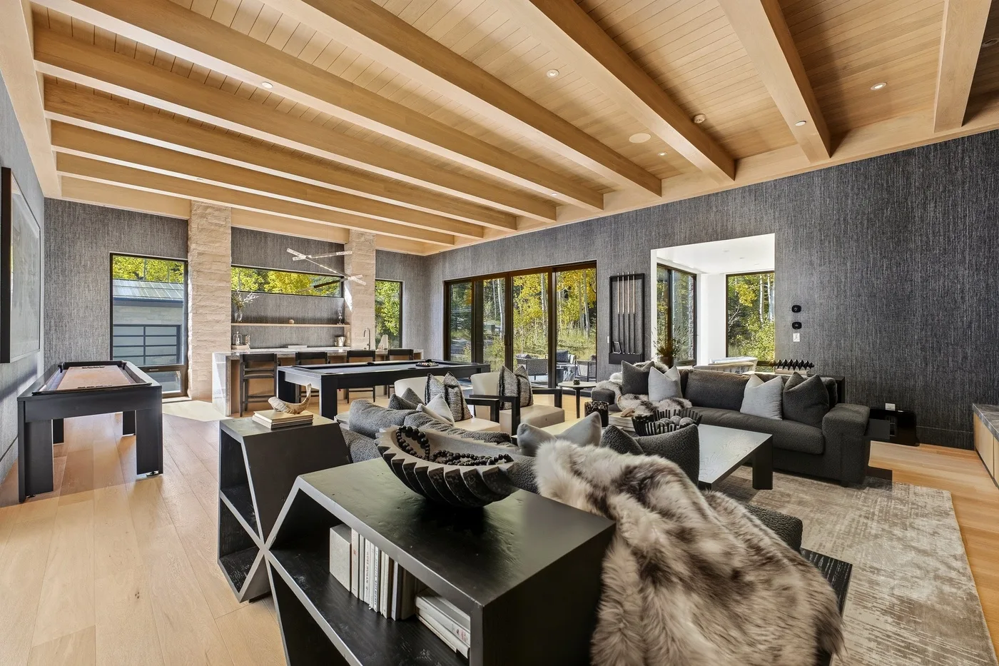 A spacious living room with dark seating beneath a vaulted wood ceiling.