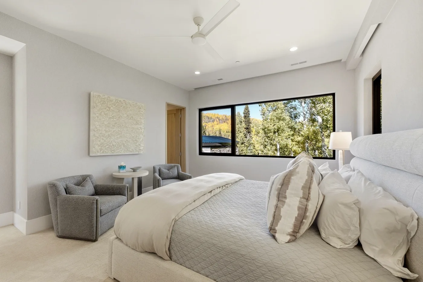 A bright bedroom with a large bed, seating area, and a wide window.