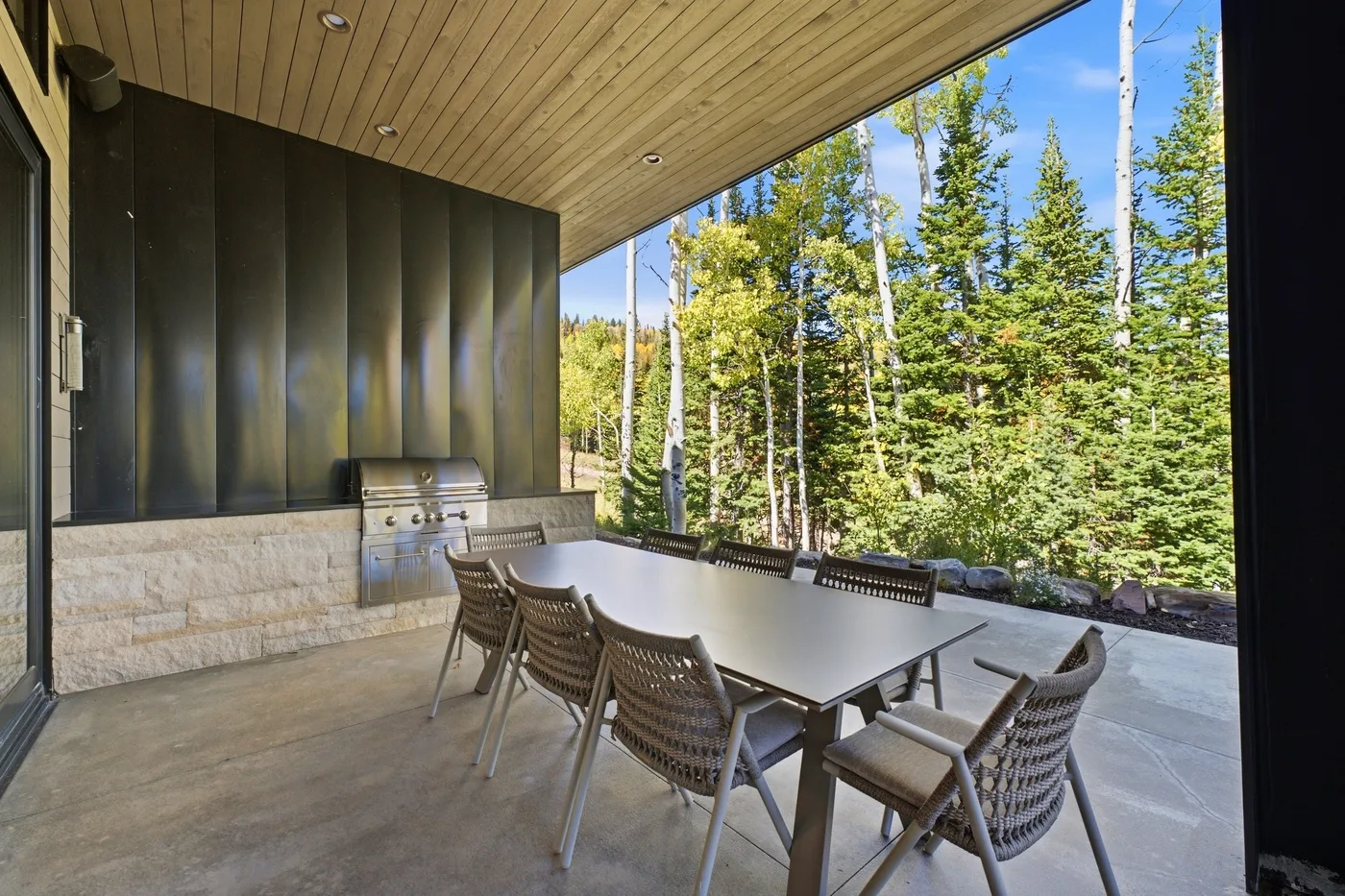 Covered outdoor dining area with a long table overlooking a wooded landscape.