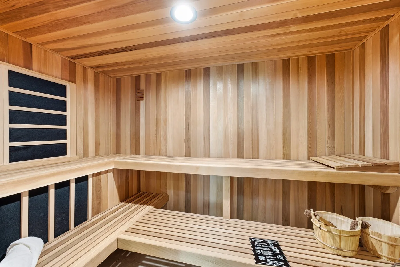 A wood-paneled sauna with tiered benches and a bucket.