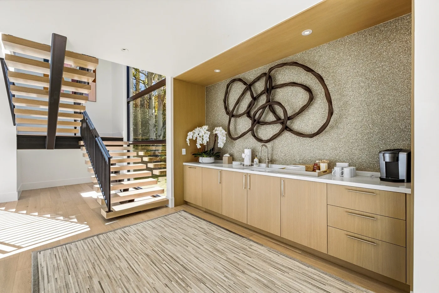 A bright interior features an open staircase beside a long wooden counter.