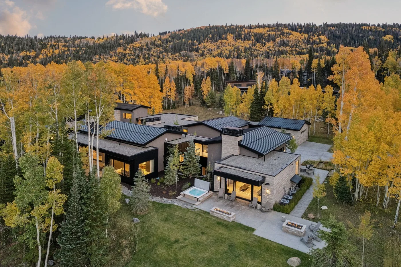 A modern building sits among autumn trees, with a forested hillside behind it.