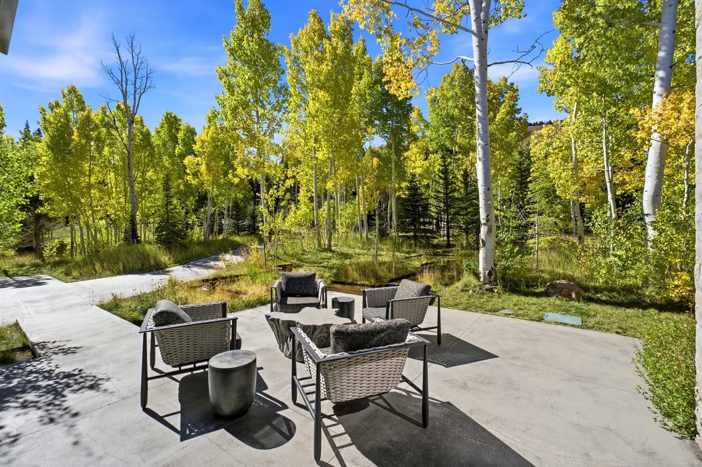 An outdoor patio with seating faces a wooded area.