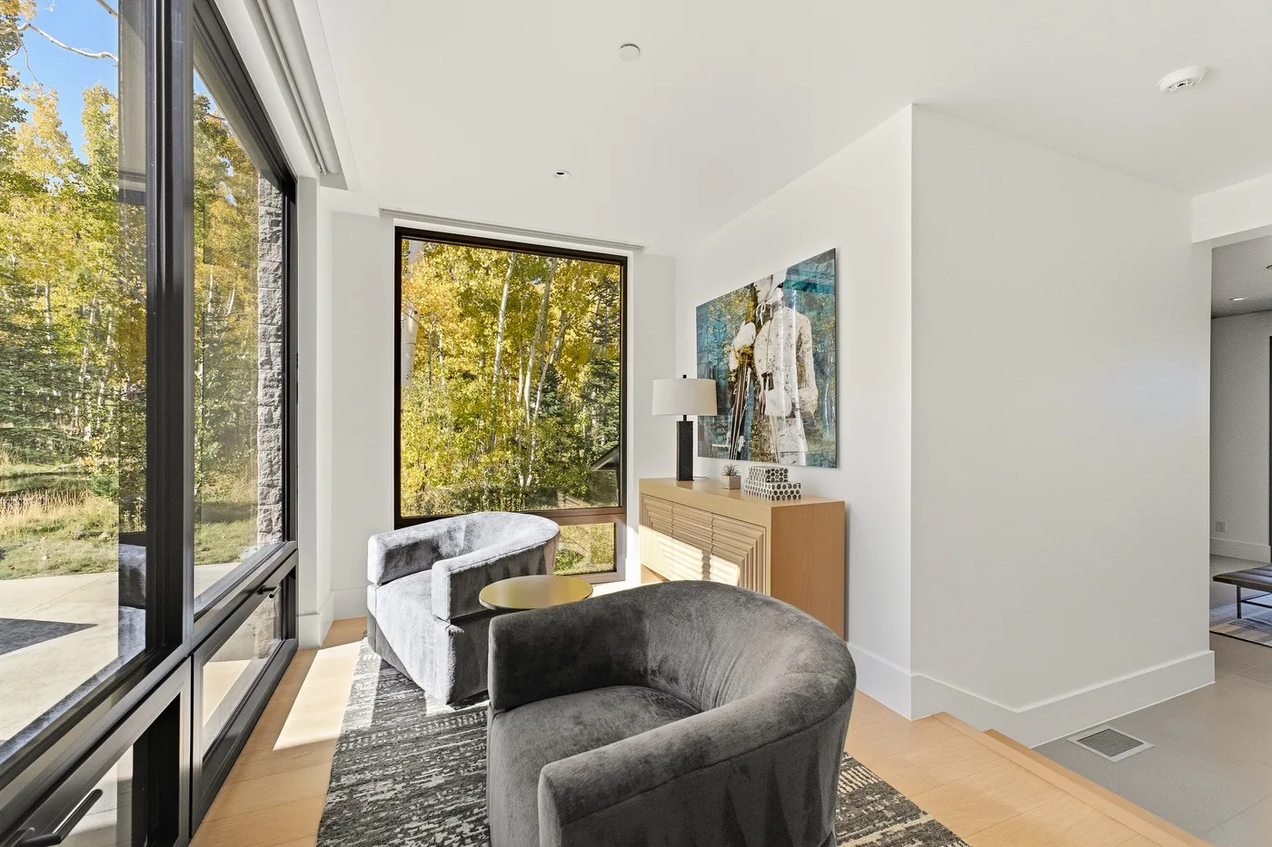 A bright living area with large windows, seating, and a cabinet beneath wall art.