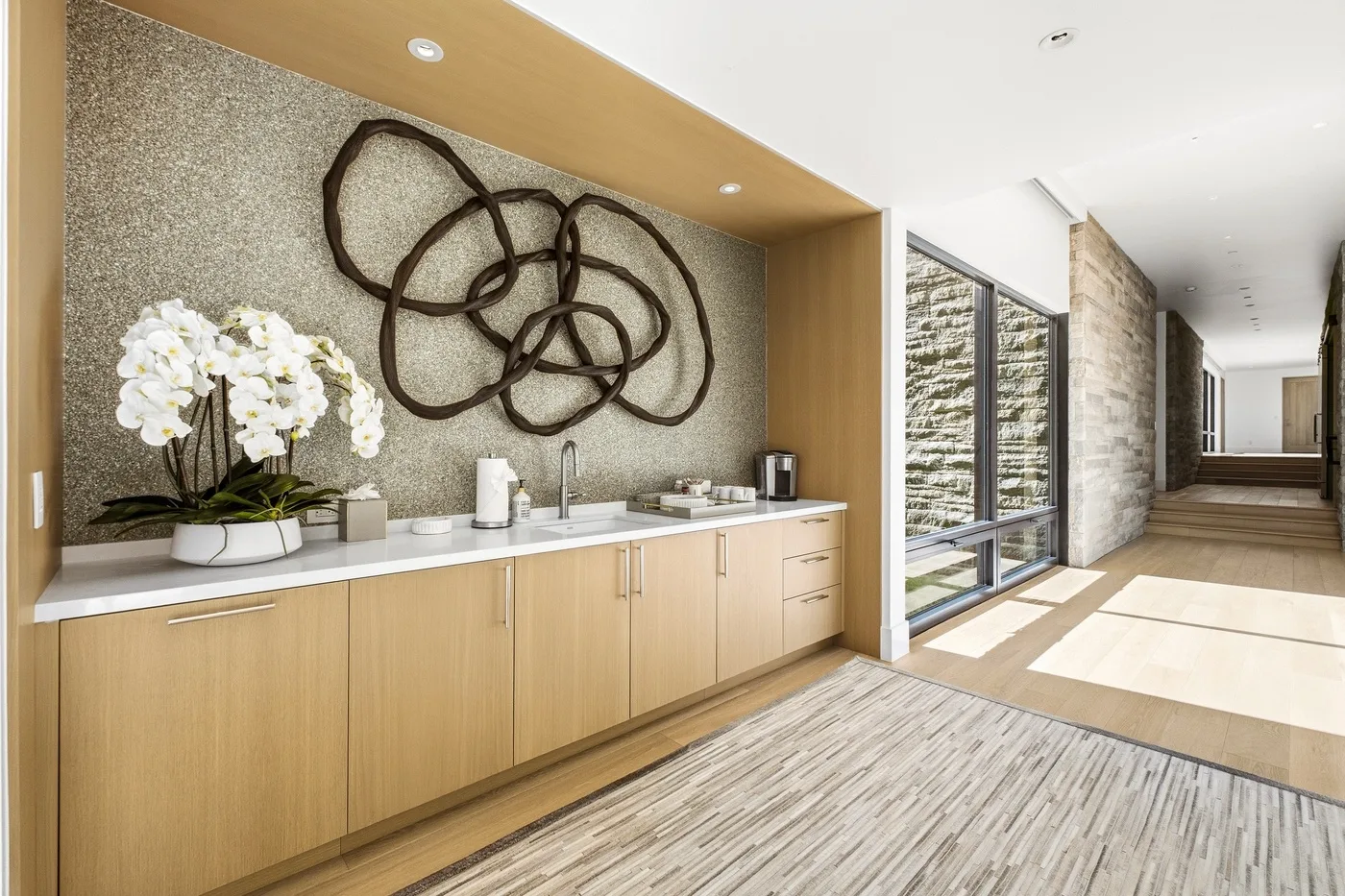 A bright hallway features a long wooden console, white flowers, and abstract wall art.