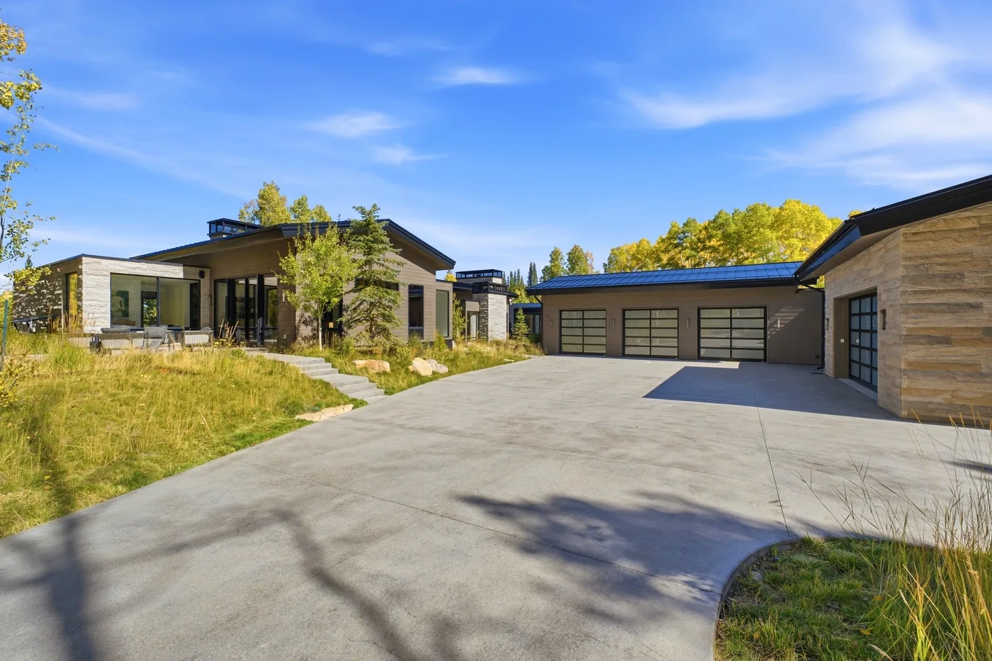 A modern house and garage face a broad paved driveway.