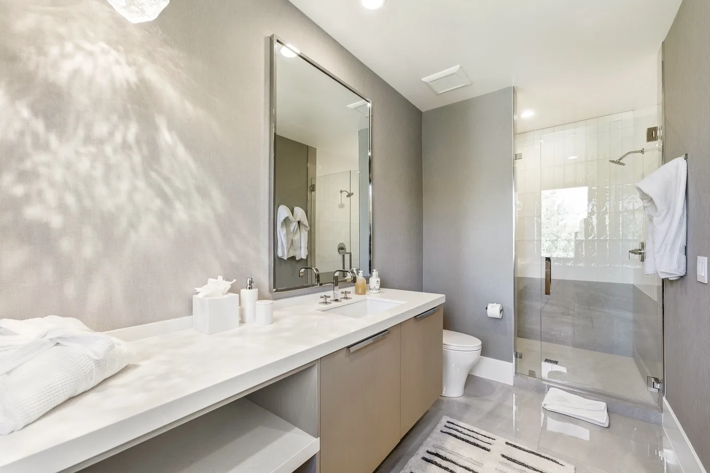 A bright bathroom with a long vanity, mirror, and glass shower.