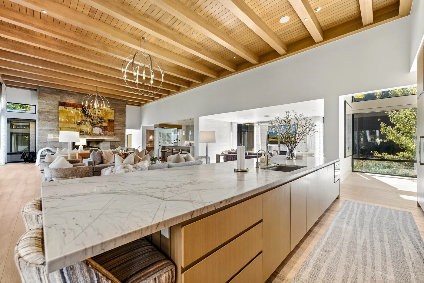 An open-plan living room and kitchen with a large island beneath a timber ceiling.