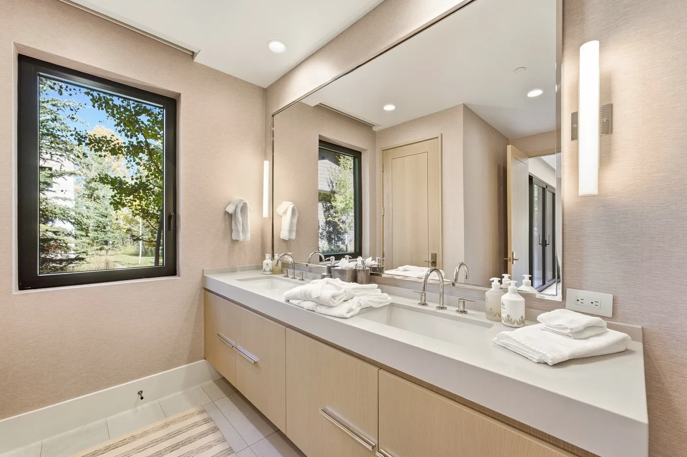 A bathroom vanity with a wide mirror and a window overlooking trees.