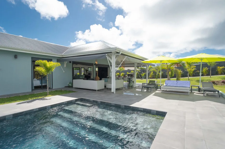 A covered patio overlooks a swimming pool, with lounge seating and bright umbrellas.