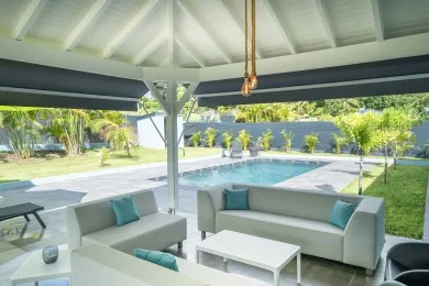 An open-air covered patio with seating faces a swimming pool.