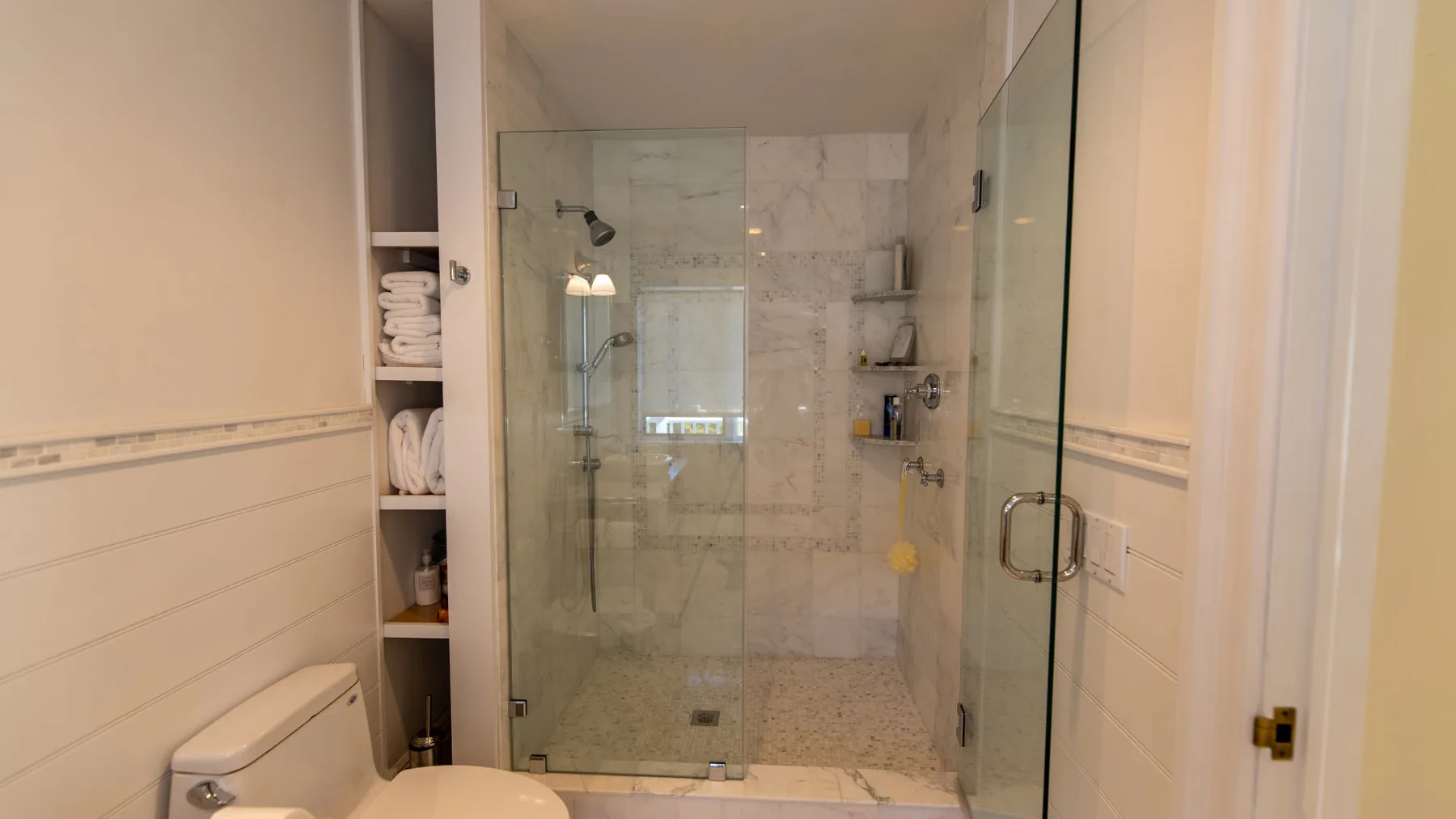 Un baño con una ducha de vidrio y estantes empotrados.