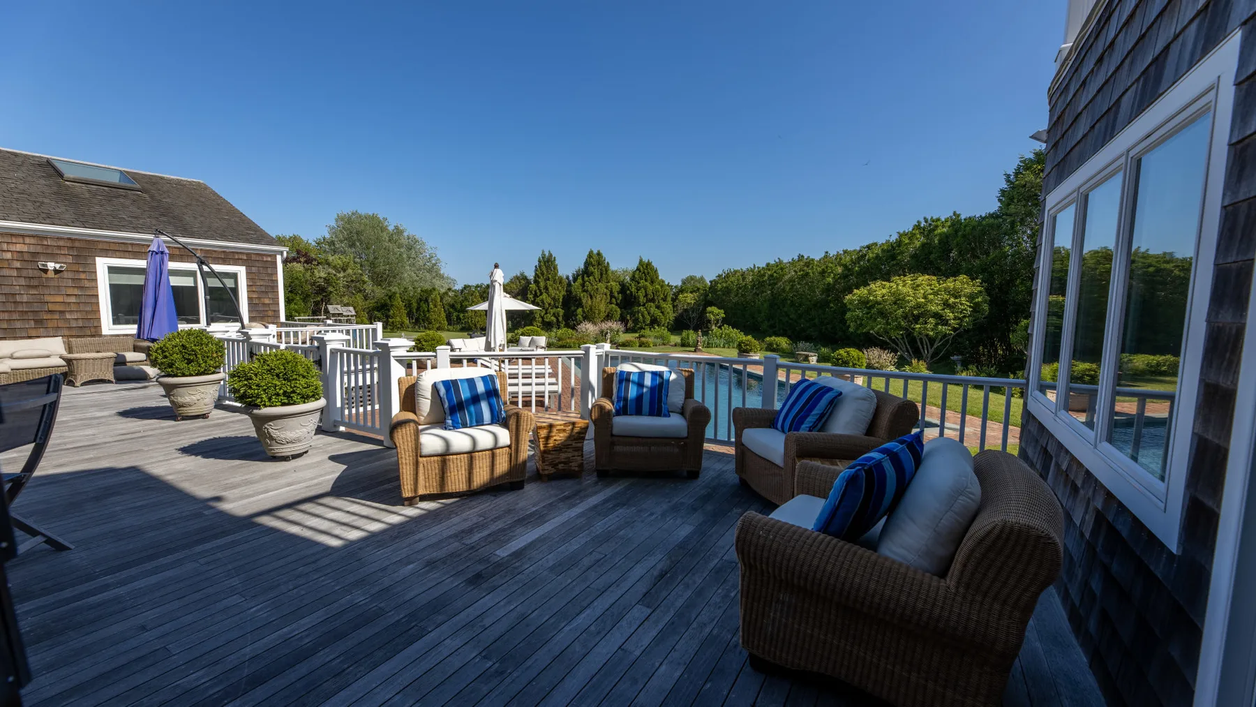 Una terraza exterior tiene asientos con cojines azules junto a una piscina cercada.