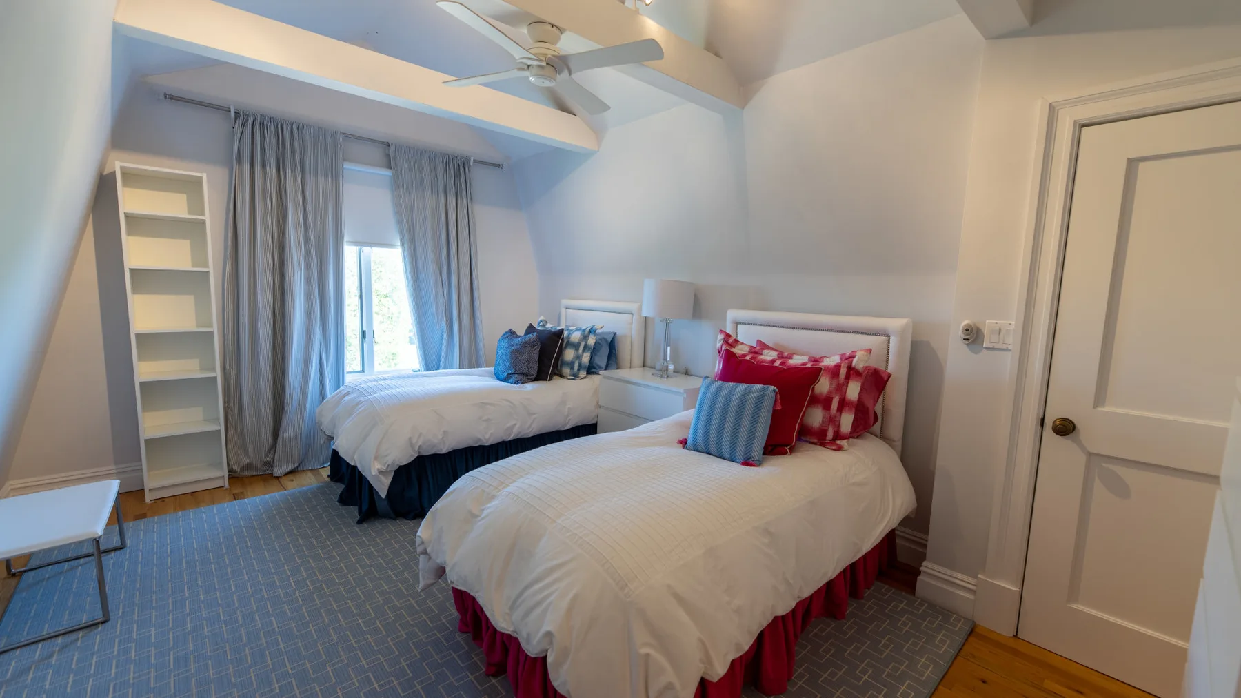 Un dormitorio con dos camas, ventanas con cortinas y un ventilador de techo.