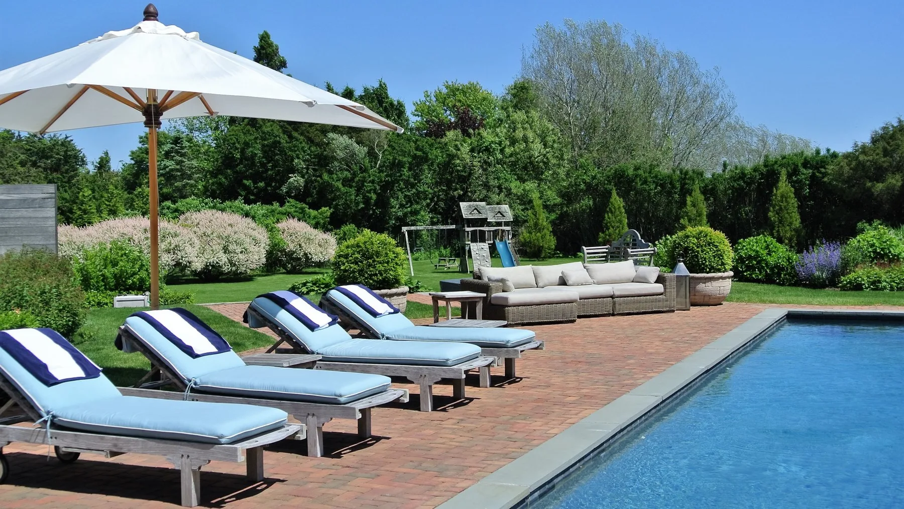 Un patio con piscina al aire libre, asientos reclinables y una gran sombrilla blanca.