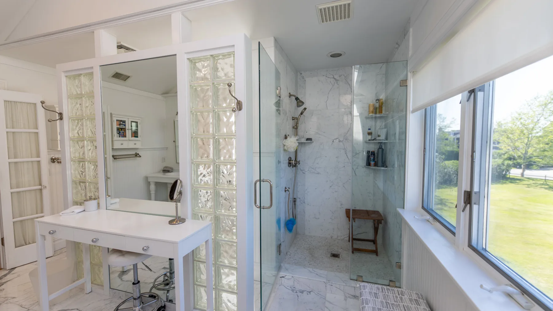 Un baño luminoso con una ducha de vidrio y una ventana amplia.
