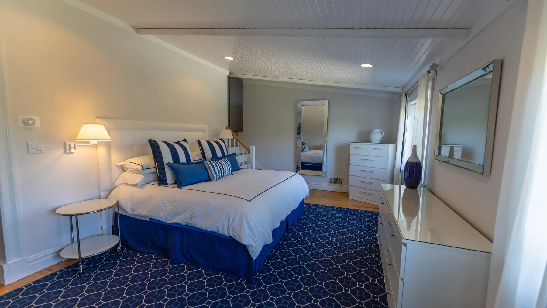 Un dormitorio con una cama bien tendida y una alfombra azul estampada.