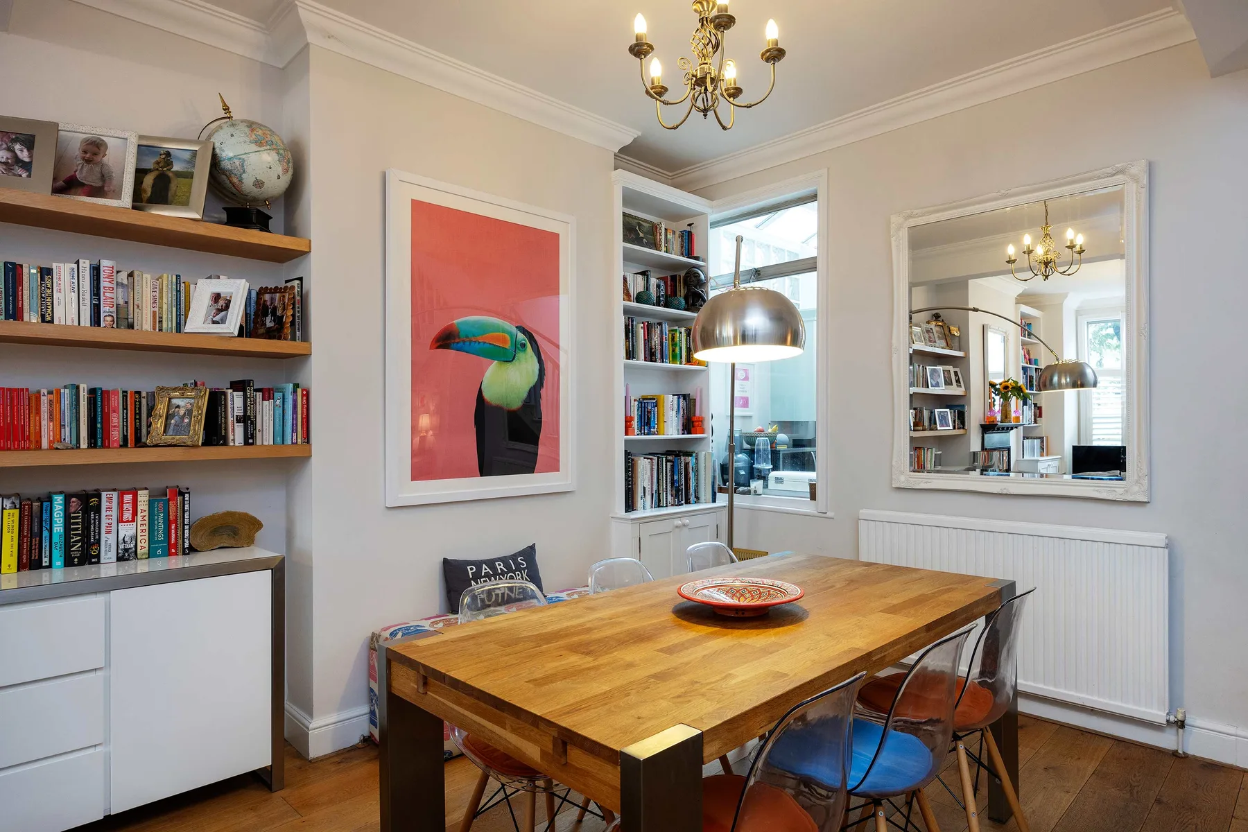 A dining area with a wooden table, bookshelves, and colorful wall art.