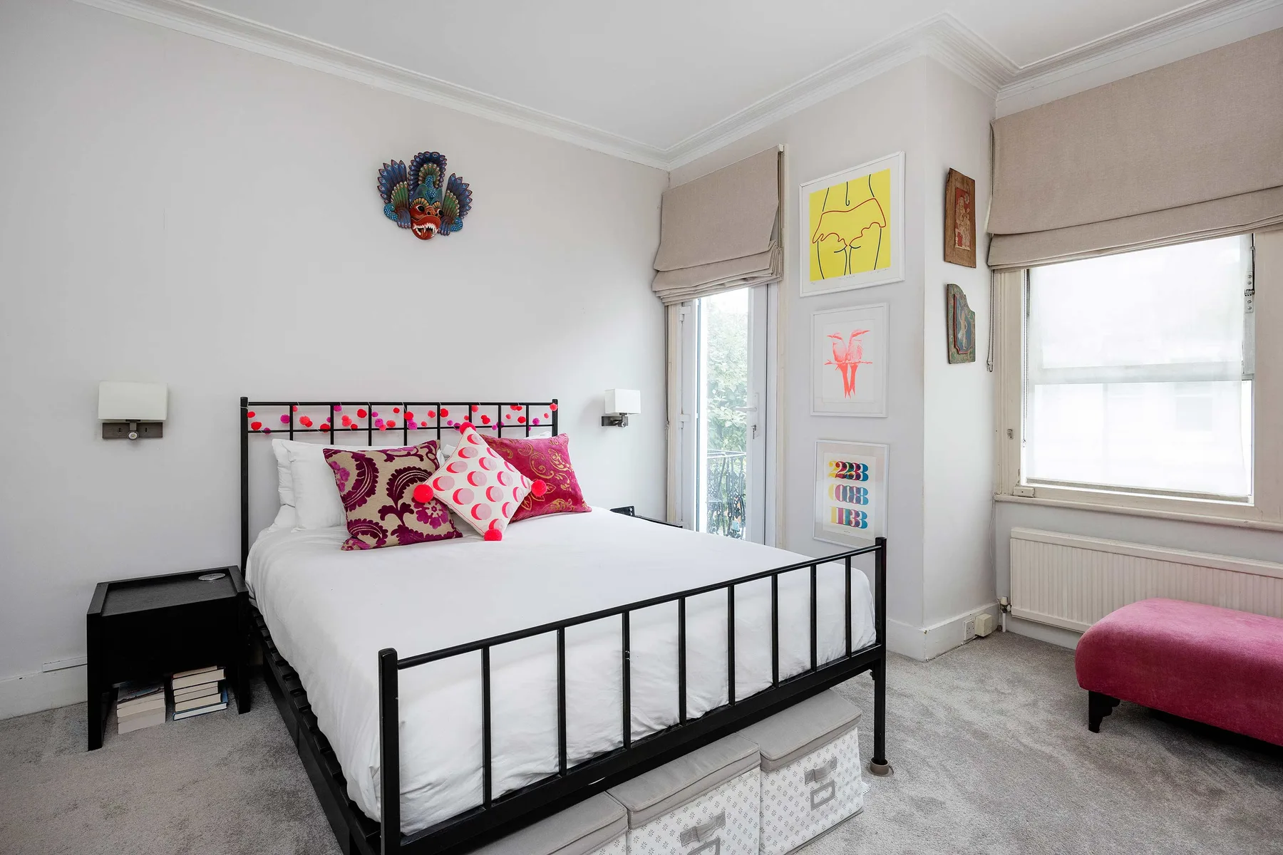 A bright bedroom with a black metal bed and colorful artwork on the walls.