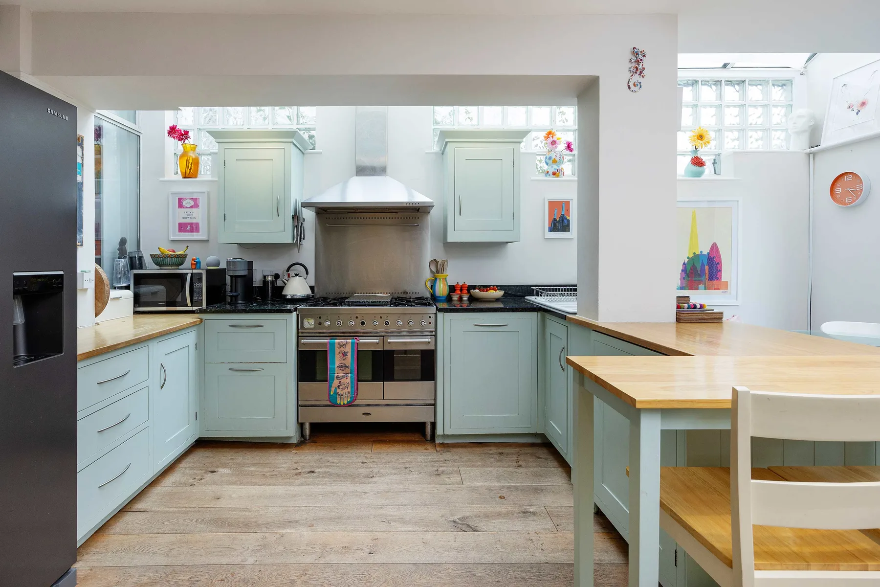 A bright kitchen with pale cabinets, a stove, and a wooden dining table.