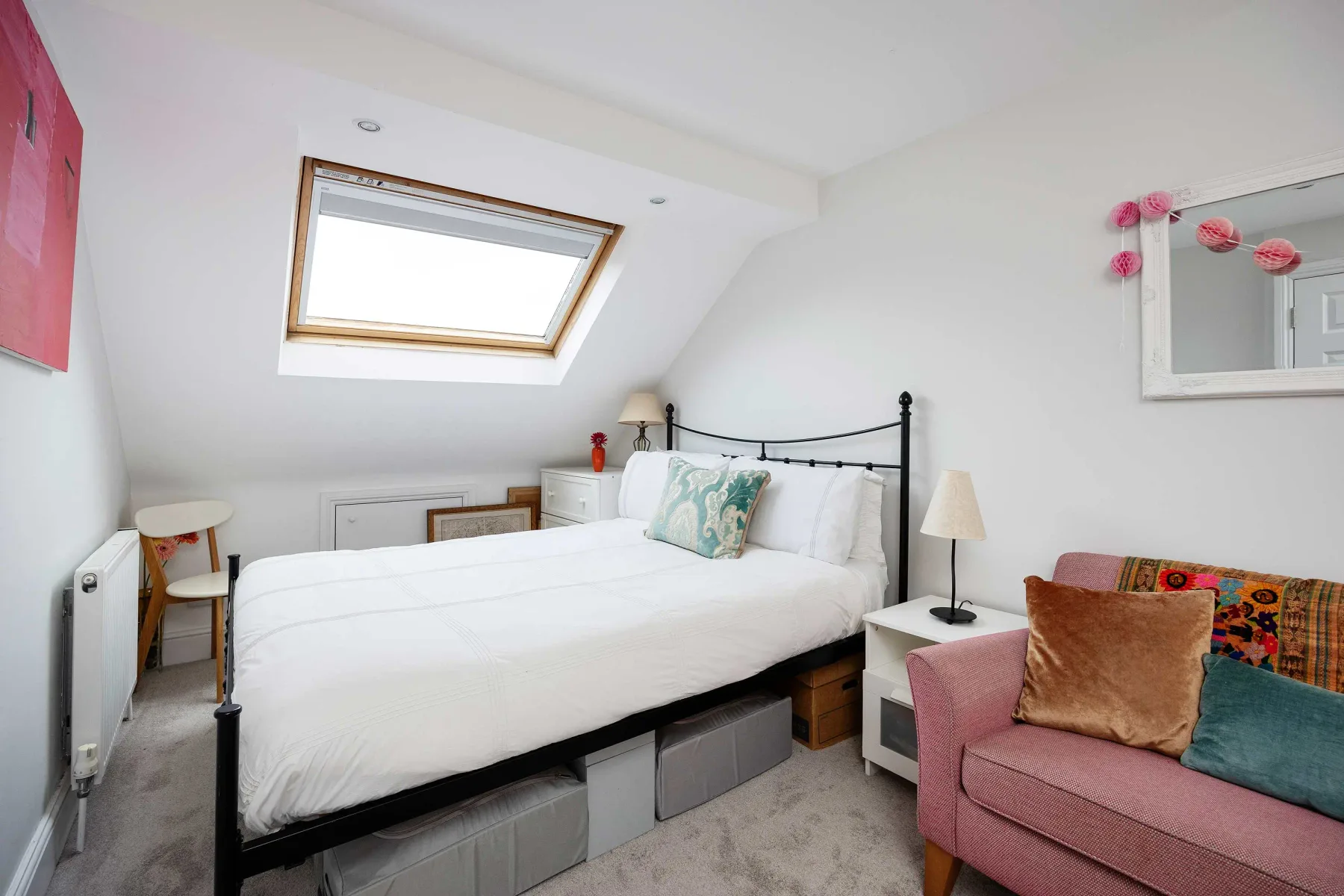 A bright bedroom with a white bed and a pink seating area.
