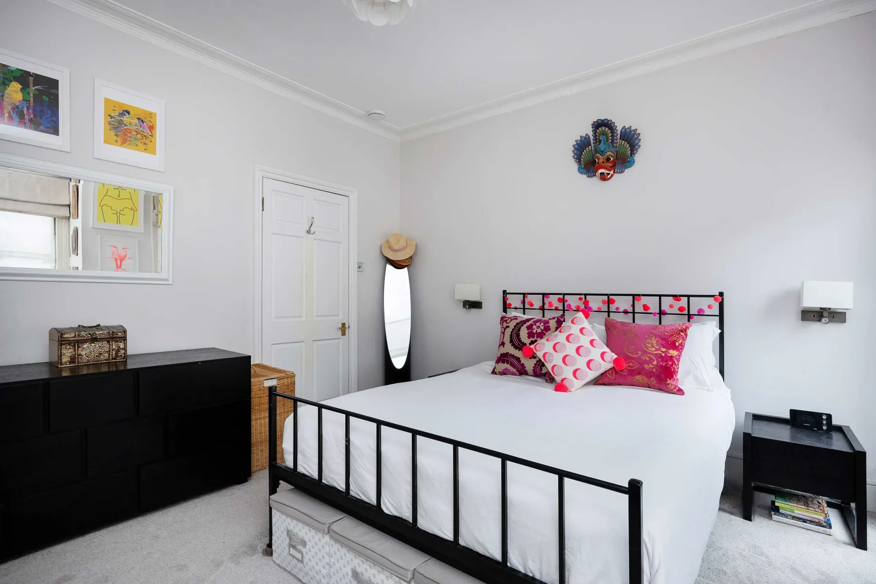 A bright bedroom with a white bed, colorful pillows, and framed artwork.