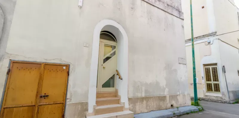 Una pared exterior con una entrada arqueada y una puerta amarilla al lado.