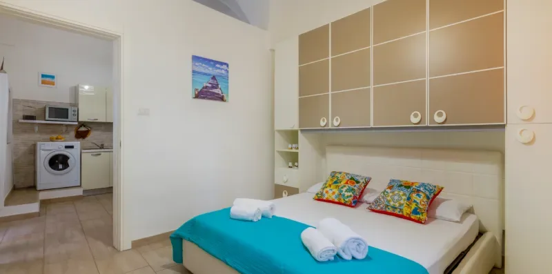 Un dormitorio con una cama vestida con ropa de cama turquesa y almohadas coloridas.
