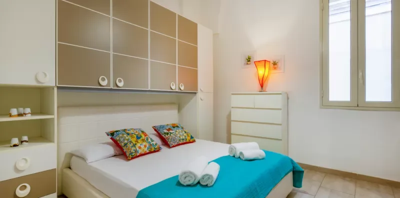 Un dormitorio con una cama vestida de blanco y turquesa bajo armarios empotrados.