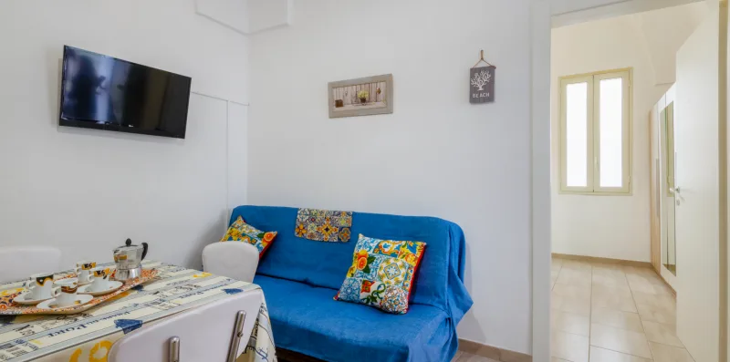 A living room with blue seating, a wall-mounted television, and a dining table.