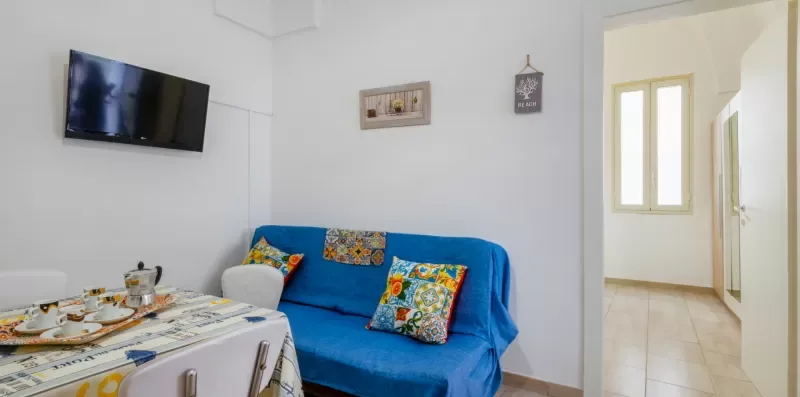Una sala de estar con asientos azules, un televisor en la pared y una mesa de comedor.