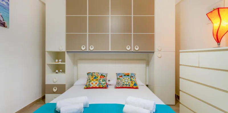 Un dormitorio con una cama, cojines coloridos y estanterías empotradas.