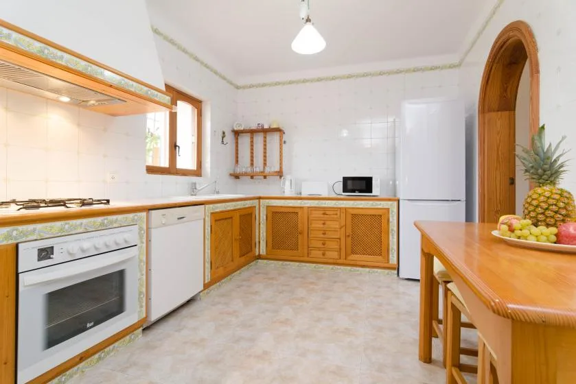 A bright kitchen with wooden cabinets, appliances, and a dining table.