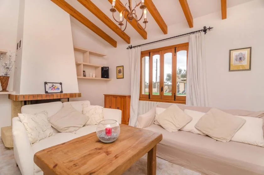 A bright living room with pale seating, a wooden coffee table, and exposed ceiling beams.