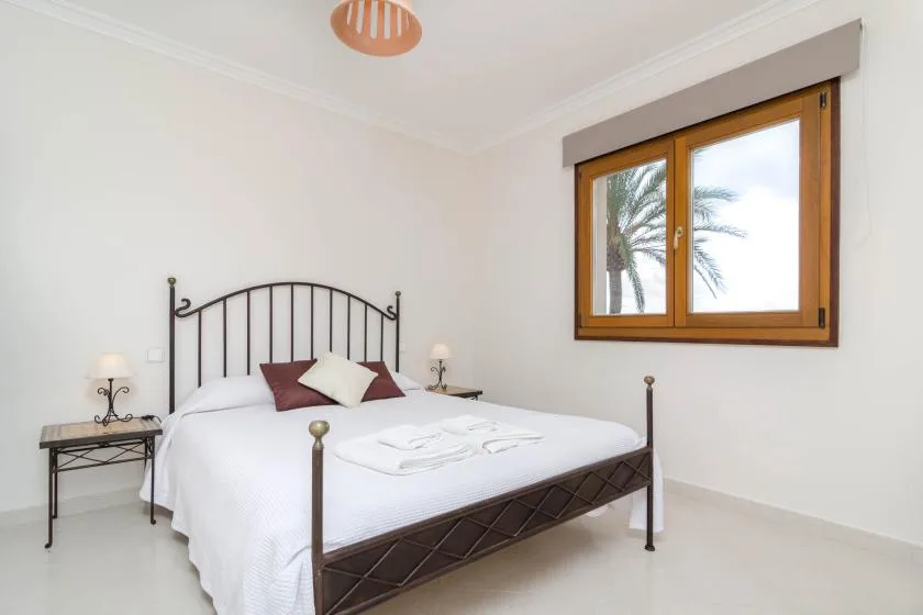 A bright bedroom with a metal bed and a wood-framed window.