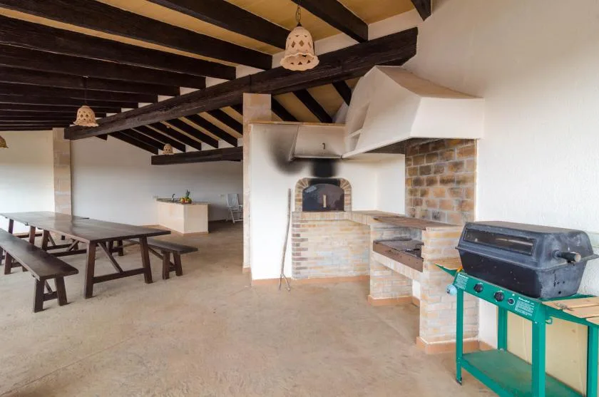 A rustic indoor dining and cooking area with a long wooden table and brick oven.