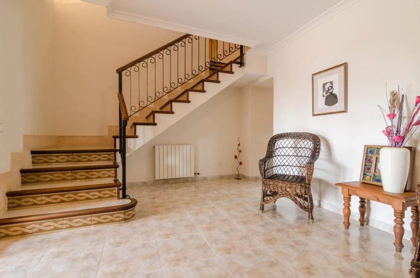 A tiled entry hall features a staircase with a decorative railing and a wicker chair.