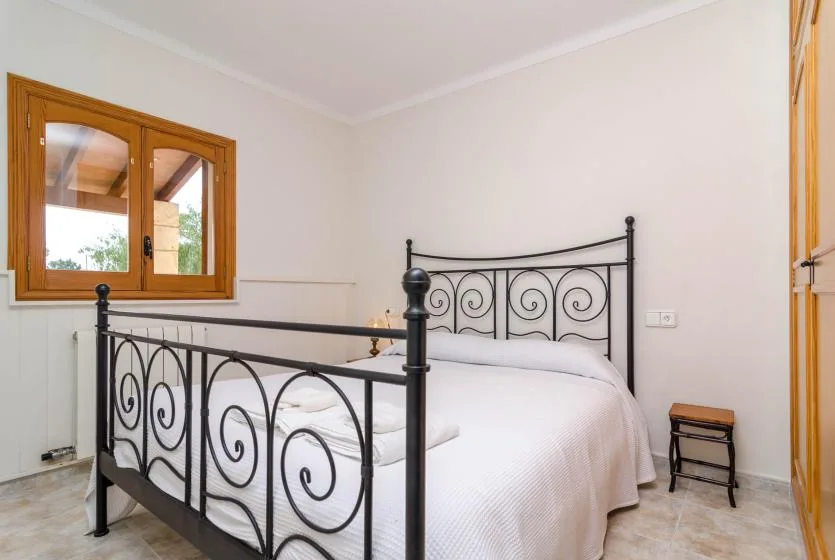 A bedroom with a white bed and black metal frame beside a wooden-framed window.