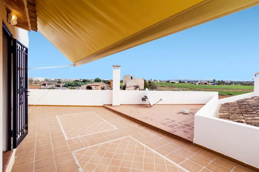 A tiled terrace with a large shade canopy overlooks open fields.
