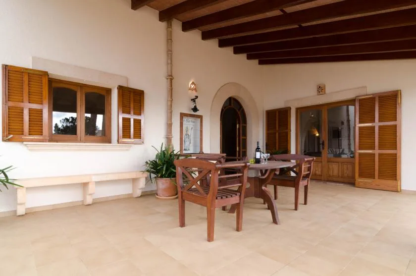 A covered dining area with a wooden table and windows along the walls.