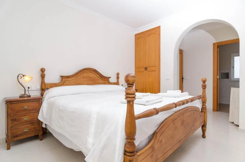 A bedroom with a wooden bed and white bedding beside an arched doorway.