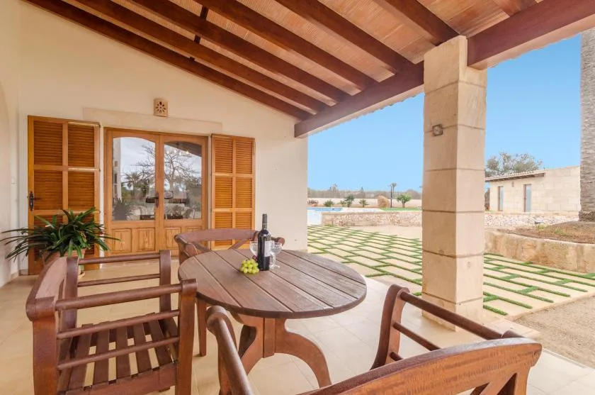 A covered outdoor dining area with a wooden table and chairs overlooks a landscaped courtyard.