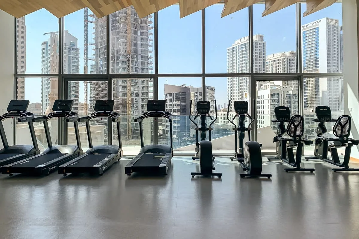 Un gimnasio con cintas de correr y bicicletas estáticas frente a grandes ventanales.