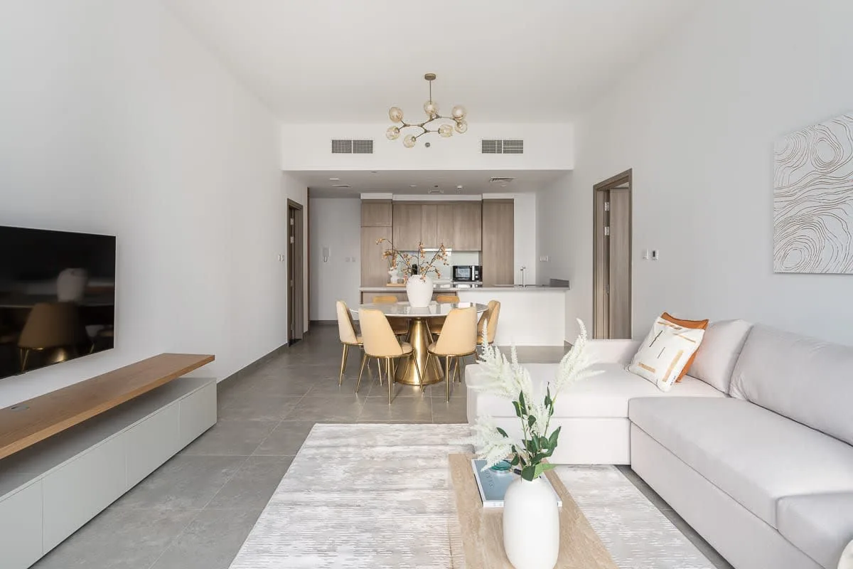 A bright living and dining area opens onto a kitchen, with a sofa and dining table.