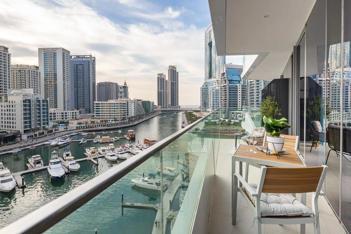 Un balcón da a una marina y edificios de la ciudad, con asientos junto a la baranda de vidrio.