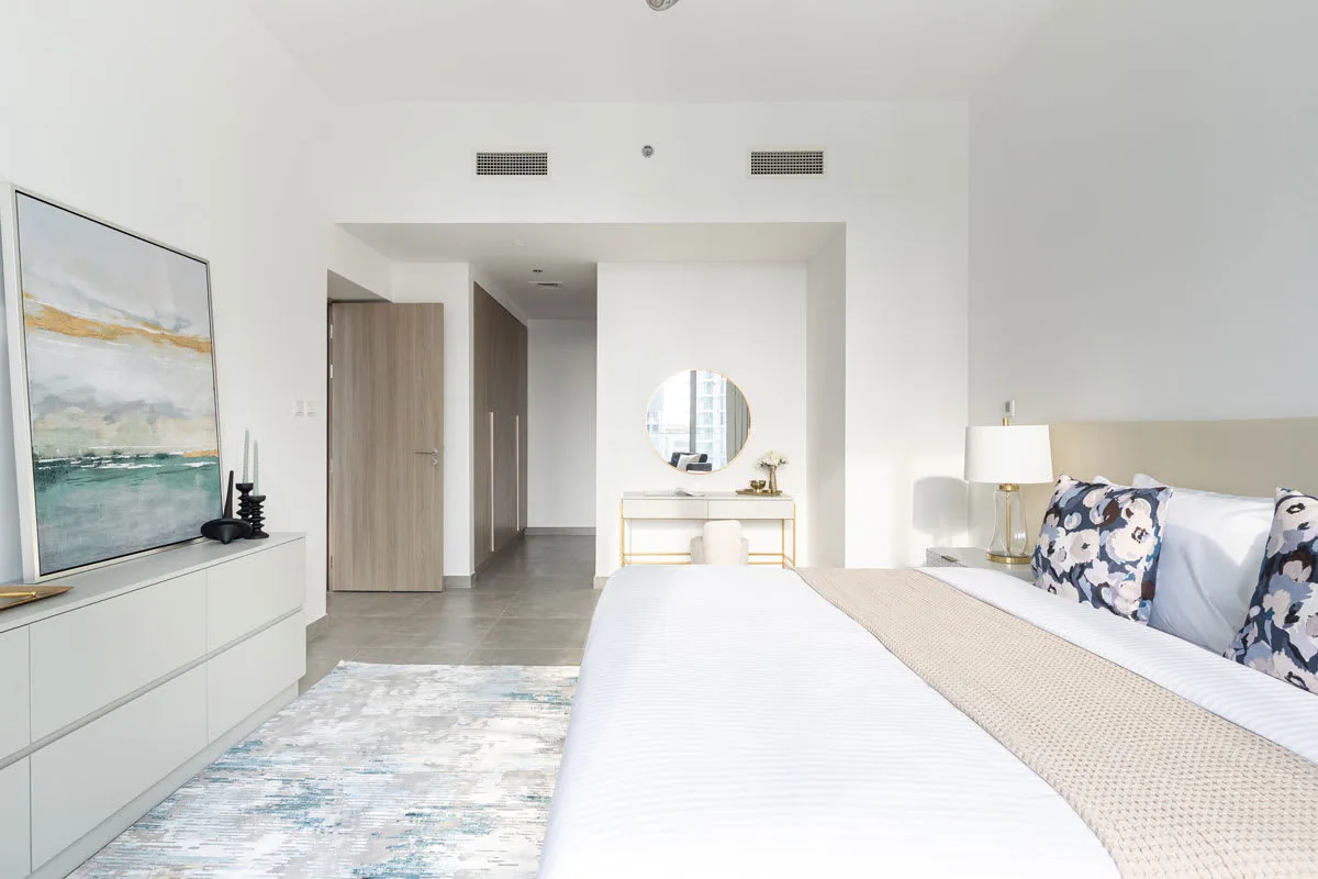 Un dormitorio luminoso con una cama grande, lámparas de noche y una obra de arte sobre una cómoda.