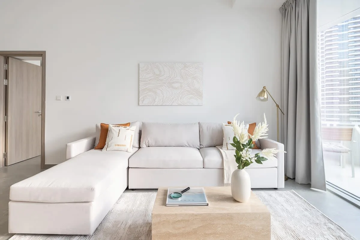 Una sala luminosa con sofá seccional, mesa de centro y grandes ventanales.