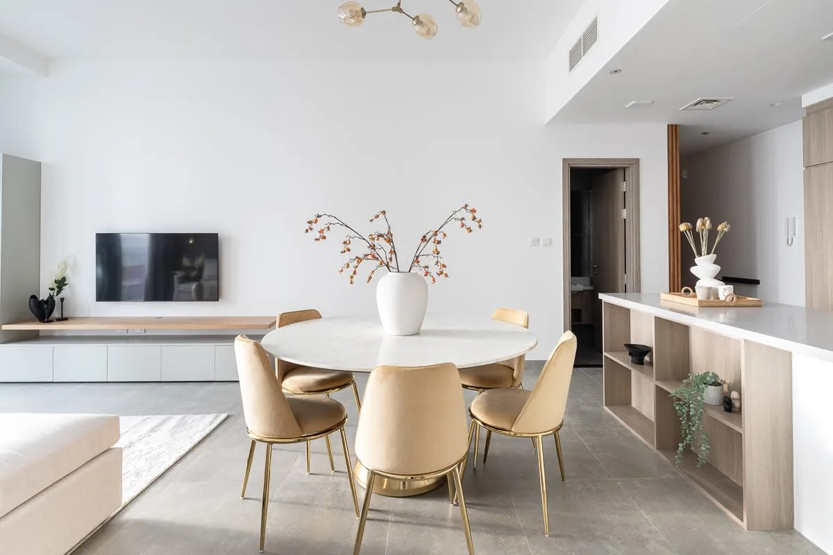 A bright dining area with a round table and a television on the wall.