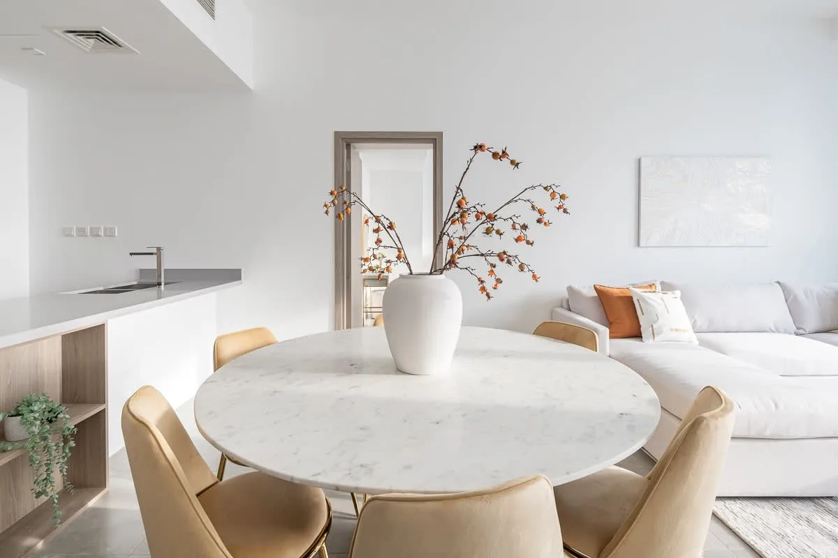 Un comedor luminoso con una mesa redonda y una zona de estar blanca detrás.