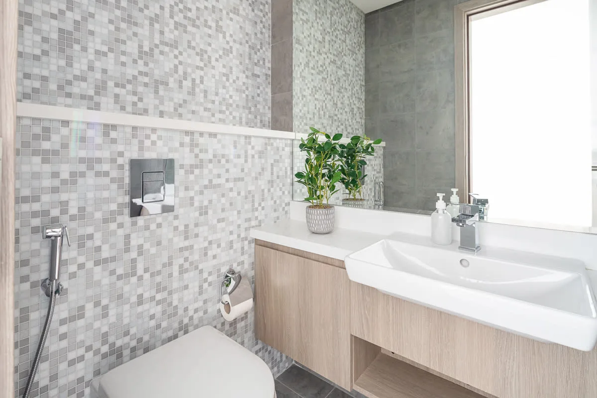 Un baño con azulejos, inodoro, lavabo con mueble y una planta en maceta.